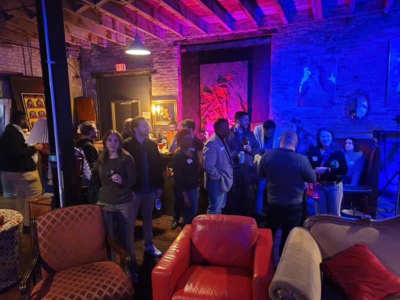 Attendees mingling at a networking event inside a dimly lit brick-walled venue with blue and red ambient lighting