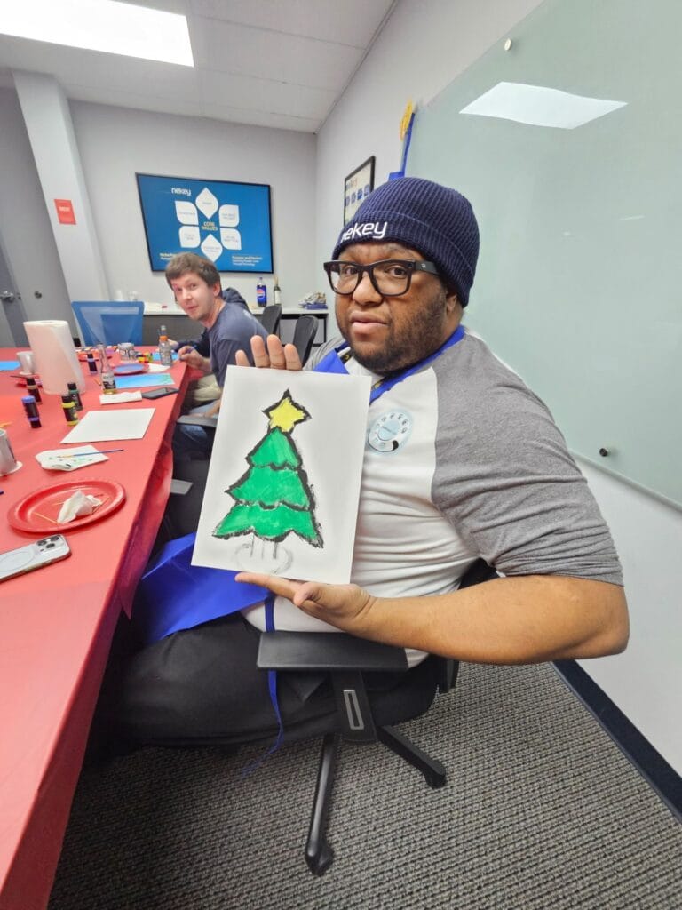 Chris Gittings holding up a hand-painted Christmas tree at a Culture Club paint and sip event