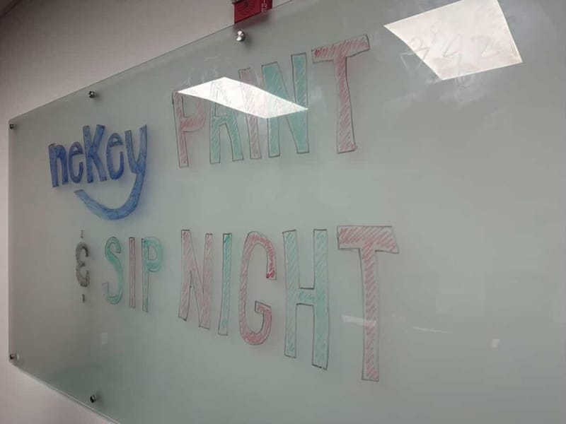 Glass whiteboard with "neKey Paint and Sip Night" written in colorful marker lettering, with the neKey logo in blue on the left