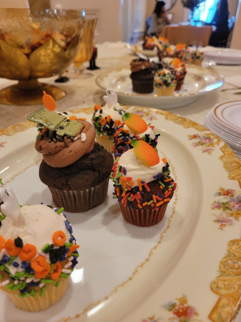 Halloween-decorated cupcakes on a vintage china plate, with orange, green, and black sprinkles and candy carrot toppers